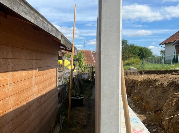 Betonfertigelemente zur Abgrenzung einer Baugrube neben Holzhaus