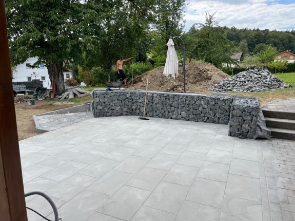 Moderne Gabionen-Sitzmauer mit großzügiger Pflasterfläche